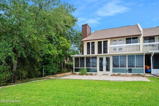 rear view of house featuring a shingled roof, a sunroom, a chimney, french doors, and a lawn