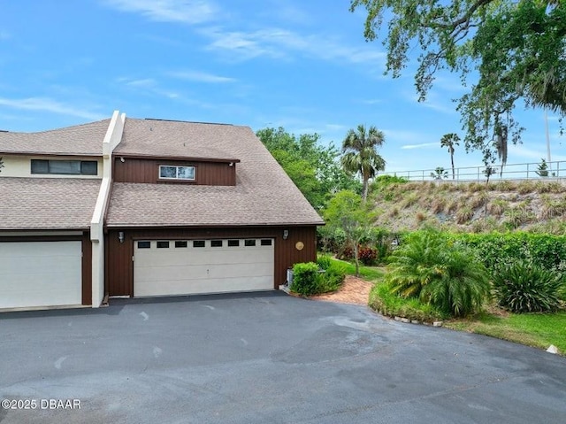 exterior space with a garage, roof with shingles, and driveway