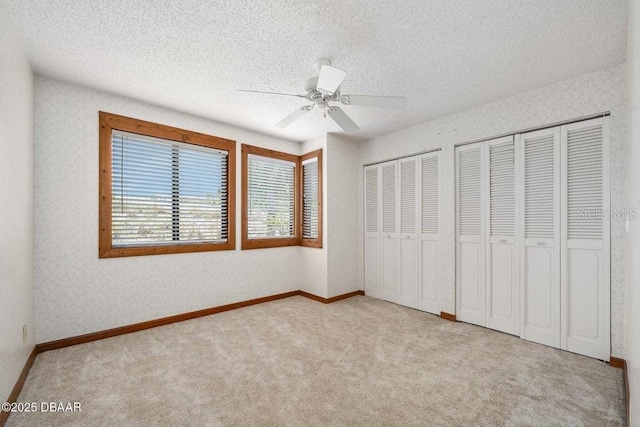 unfurnished bedroom with carpet floors, a textured ceiling, multiple closets, and a ceiling fan