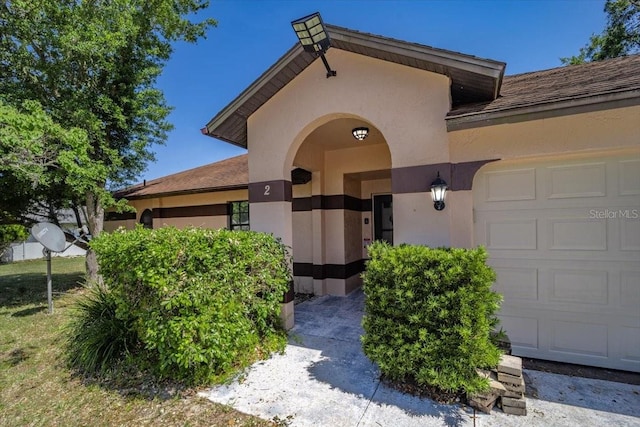 view of exterior entry with an attached garage, a shingled roof, and stucco siding
