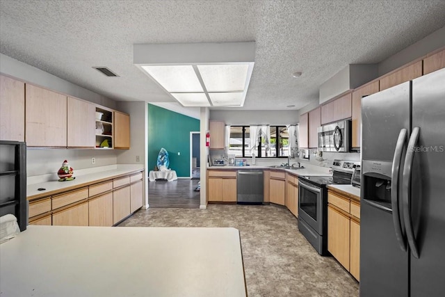 kitchen with a textured ceiling, a sink, appliances with stainless steel finishes, light brown cabinetry, and light floors