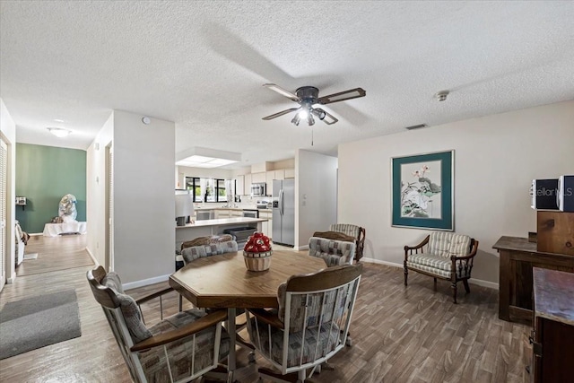 dining area featuring visible vents, wood finished floors, a ceiling fan, and a textured ceiling