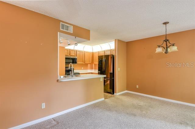 27 Catalonia Ct Unit A, Saint Augustine, FL 32086 - kitchen with freestanding refrigerator, light carpet, light countertops, stainless steel microwave, and a notable chandelier