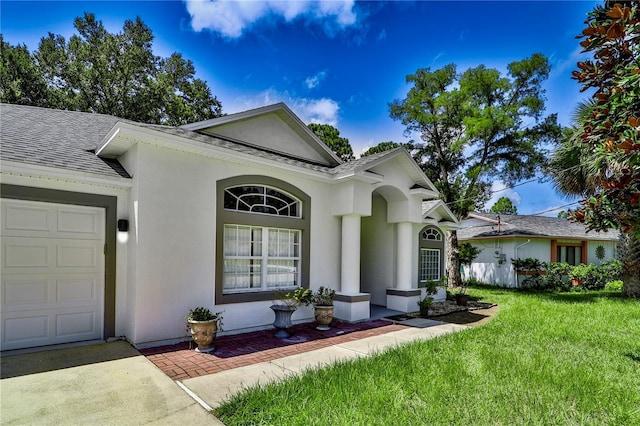 view of front of home featuring an attached garage, roof with shingles, stucco siding, and a front yard