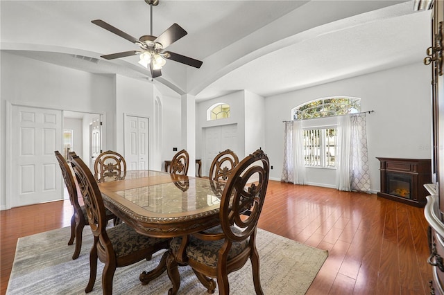 dining area with visible vents, a glass covered fireplace, wood finished floors, arched walkways, and a ceiling fan