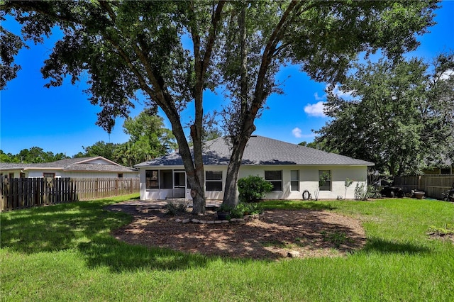 rear view of property featuring a lawn, a fenced backyard, a sunroom, and stucco siding