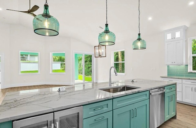 kitchen with stainless steel dishwasher, light stone countertops, light wood-style floors, white cabinetry, and a sink
