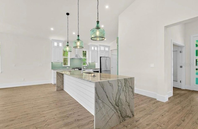 kitchen featuring freestanding refrigerator, light wood-style floors, baseboards, white cabinets, and backsplash