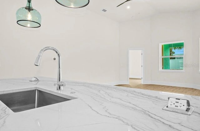 kitchen with decorative light fixtures, light wood-type flooring, a sink, light stone counters, and high vaulted ceiling