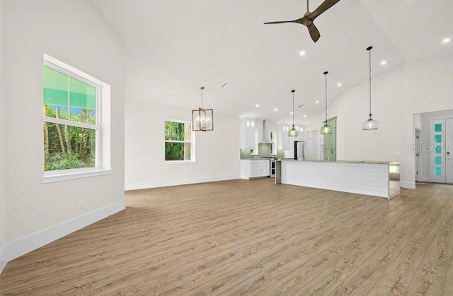 unfurnished living room with light wood-type flooring, high vaulted ceiling, baseboards, ceiling fan with notable chandelier, and recessed lighting