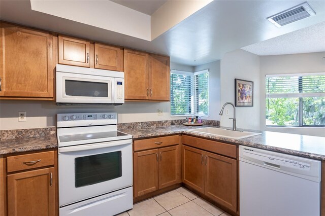 kitchen with a sink, brown cabinetry, white appliances, and visible vents