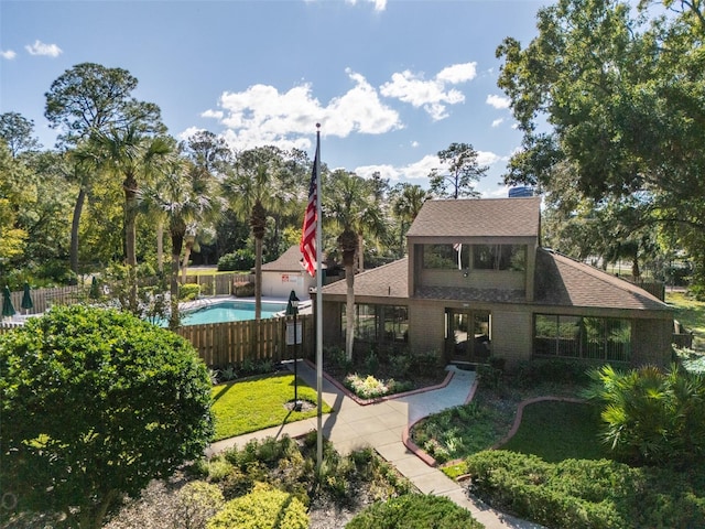 view of front facade featuring brick siding, a shingled roof, fence, and a fenced in pool