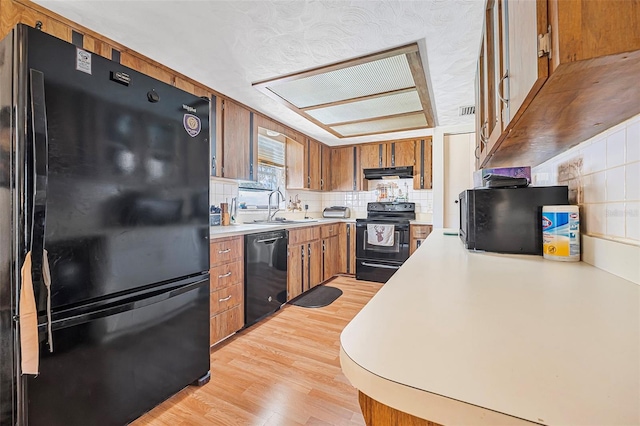 kitchen featuring range hood, brown cabinets, a sink, light countertops, and black appliances