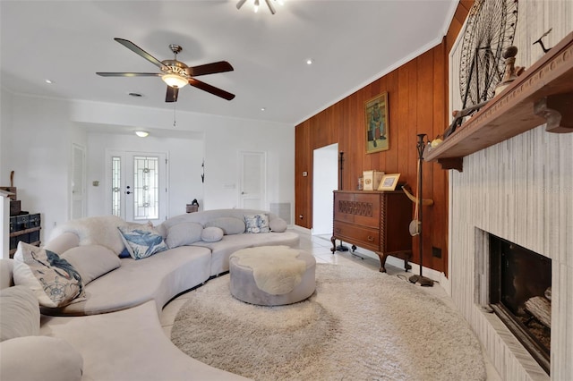 living area with wooden walls, a ceiling fan, ornamental molding, and a fireplace