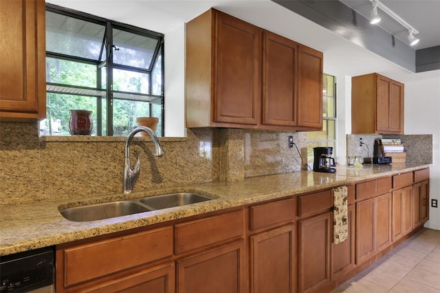 kitchen with brown cabinets, light stone counters, a sink, dishwasher, and tasteful backsplash
