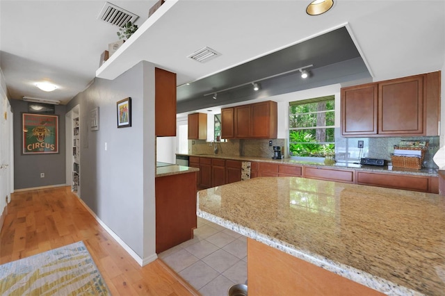 kitchen with baseboards, light stone countertops, backsplash, and visible vents