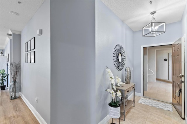 hall featuring baseboards, a textured ceiling, and a chandelier
