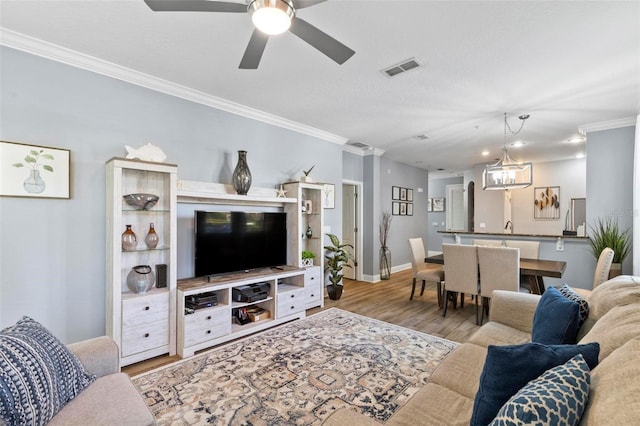 living room with baseboards, ornamental molding, wood finished floors, and visible vents