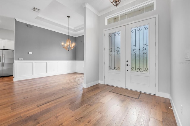 foyer entrance with crown molding, an inviting chandelier, light wood finished floors, french doors, and visible vents