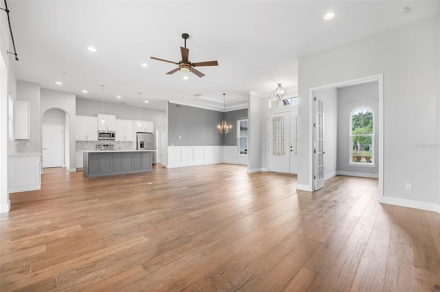 unfurnished living room with recessed lighting, arched walkways, light wood finished floors, and ceiling fan with notable chandelier