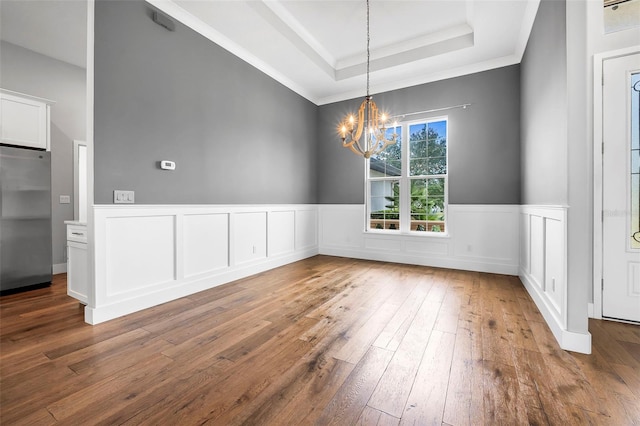 unfurnished dining area featuring an inviting chandelier, wood-type flooring, crown molding, and a tray ceiling