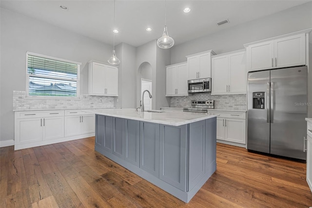 kitchen with decorative backsplash, appliances with stainless steel finishes, arched walkways, dark wood finished floors, and a sink