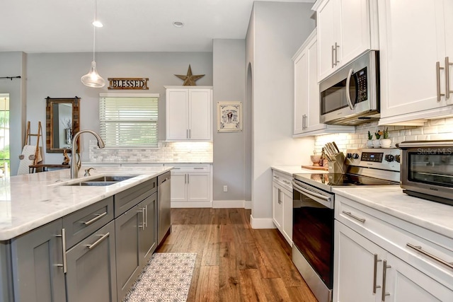 kitchen featuring white cabinets, a sink, stainless steel appliances, decorative backsplash, and gray cabinetry