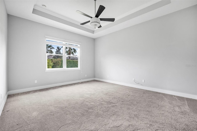 carpeted empty room featuring a tray ceiling, ceiling fan, and baseboards