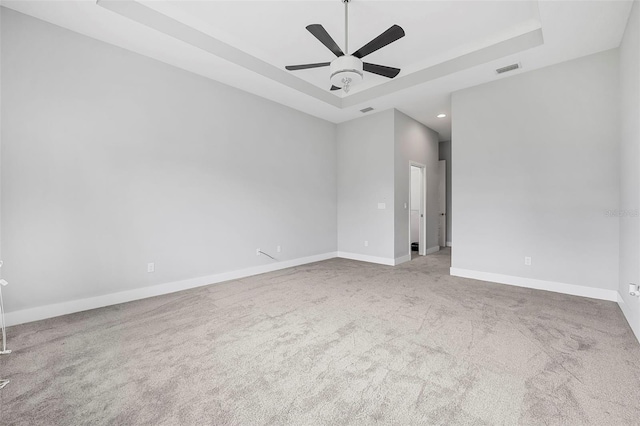empty room featuring visible vents, a ceiling fan, a tray ceiling, and carpet flooring