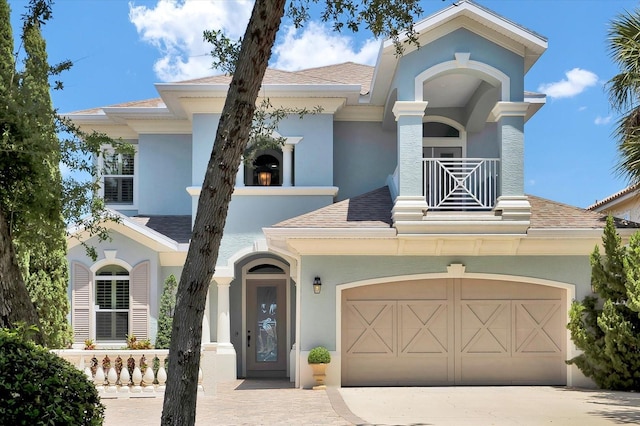 mediterranean / spanish-style home featuring roof with shingles, stucco siding, a balcony, and driveway