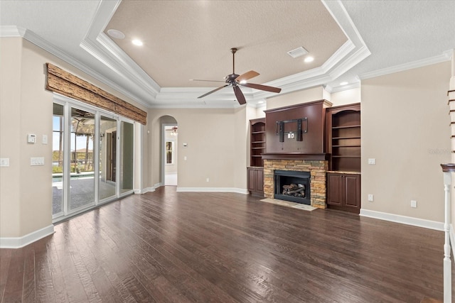 unfurnished living room with ceiling fan, a stone fireplace, crown molding, arched walkways, and dark wood-style floors