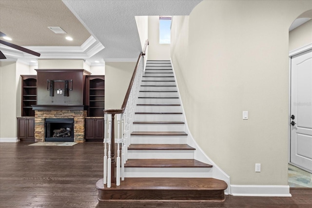 stairs featuring a stone fireplace, a textured ceiling, crown molding, wood finished floors, and recessed lighting