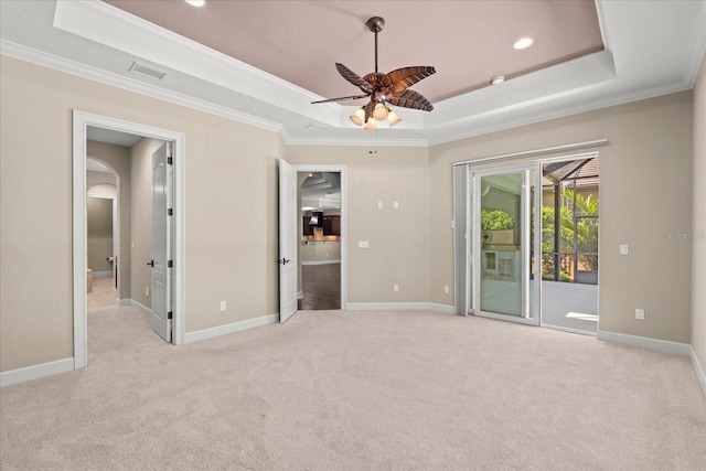 carpeted spare room with ornamental molding, a raised ceiling, a ceiling fan, and arched walkways