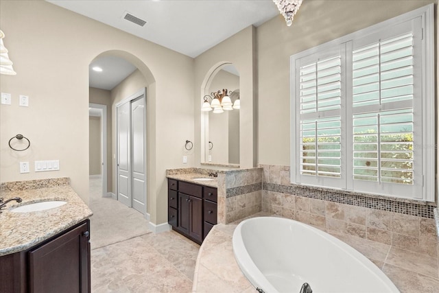 bathroom featuring visible vents, two vanities, a sink, and a garden tub