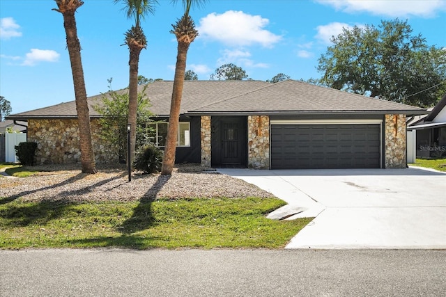 single story home featuring roof with shingles, an attached garage, driveway, and stone siding