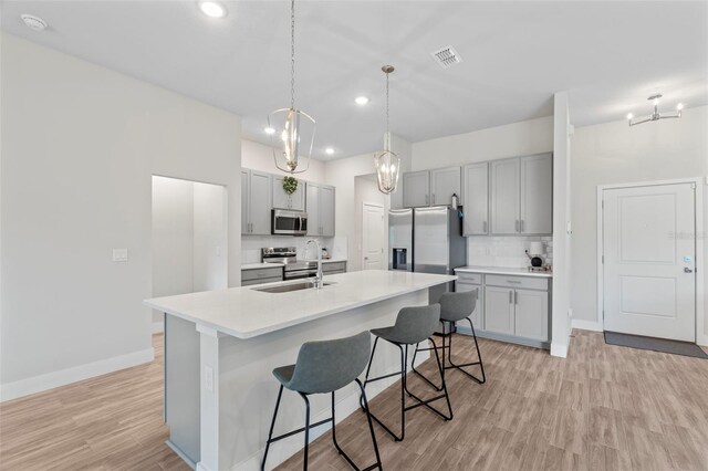 kitchen featuring a kitchen bar, light wood-type flooring, gray cabinets, appliances with stainless steel finishes, and backsplash