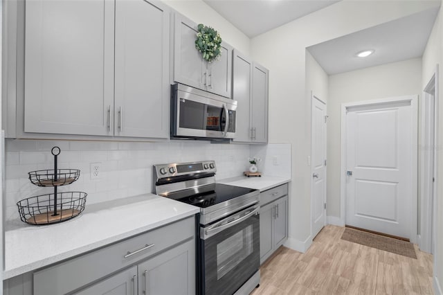 kitchen featuring decorative backsplash, gray cabinets, light countertops, light wood-style floors, and stainless steel appliances