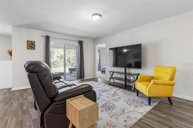 living room featuring a textured ceiling, baseboards, visible vents, and wood finished floors