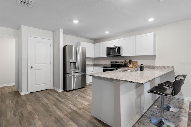 kitchen with a peninsula, wood finished floors, baseboards, a kitchen bar, and appliances with stainless steel finishes