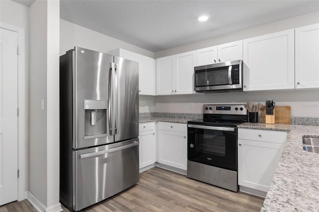 kitchen with white cabinets, light stone countertops, light wood finished floors, stainless steel appliances, and recessed lighting