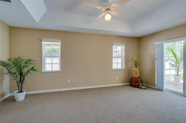 carpeted empty room with a healthy amount of sunlight, a ceiling fan, a tray ceiling, and a textured ceiling