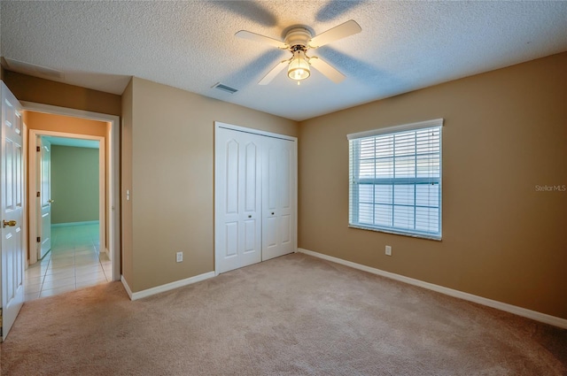 unfurnished bedroom featuring light colored carpet, a textured ceiling, visible vents, and a closet