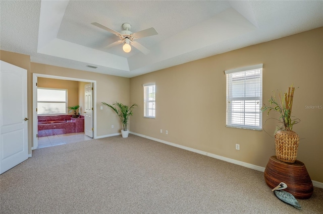 carpeted spare room featuring baseboards, ceiling fan, a tray ceiling, and visible vents