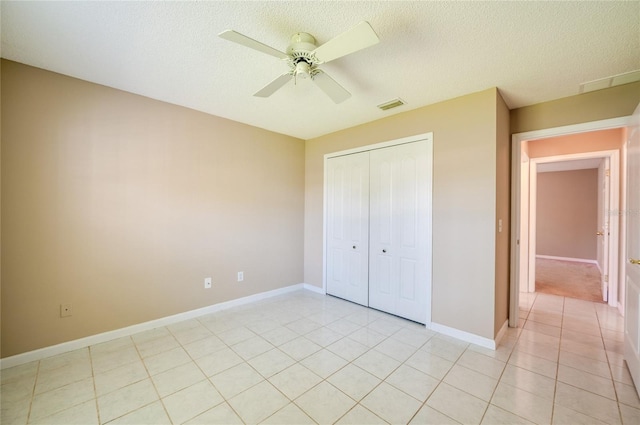 unfurnished bedroom with a textured ceiling, visible vents, light tile patterned floors, baseboards, and a closet