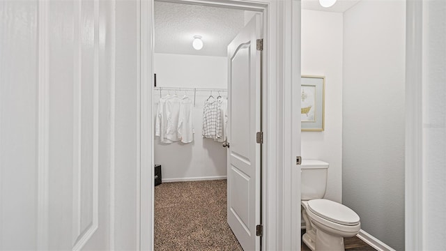 bathroom featuring baseboards, toilet, a textured ceiling, and a spacious closet