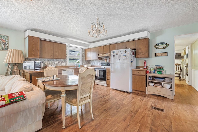 kitchen featuring under cabinet range hood, white appliances, light wood-style flooring, and visible vents
