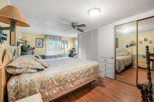 bedroom with two closets, a ceiling fan, a textured ceiling, and wood finished floors
