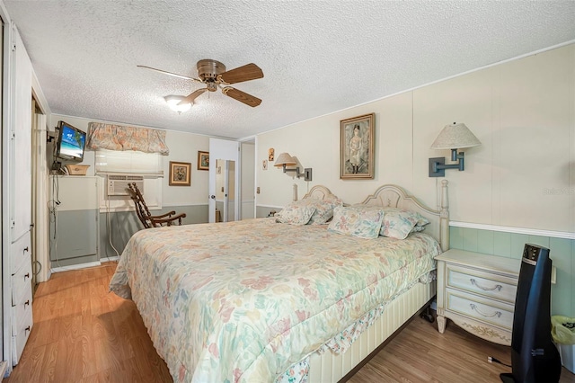 bedroom with a ceiling fan, a textured ceiling, wainscoting, and wood finished floors