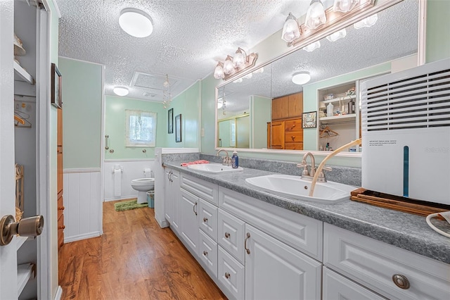 bathroom featuring a sink, wainscoting, toilet, and a textured ceiling