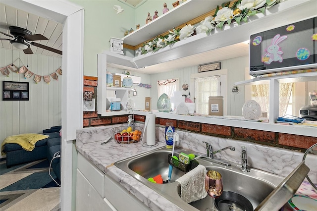 kitchen with ceiling fan, open shelves, wood walls, a sink, and white cabinetry